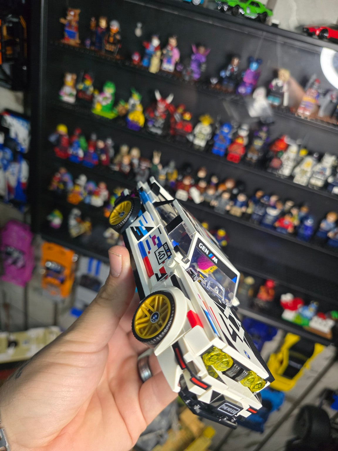 Built LEGO Speed Champions BMW M3 E30 held in hand with display shelves behind